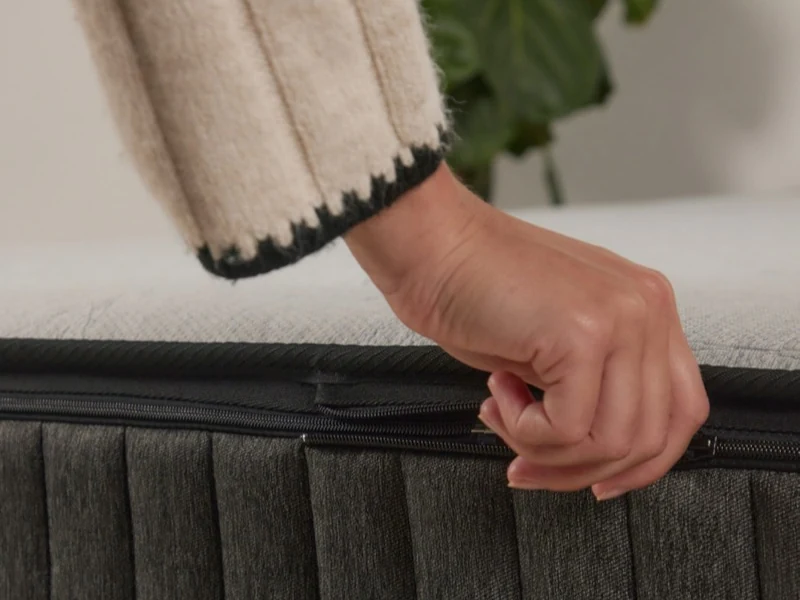 A hand opening the zip on an Ausbeds mattress cover.